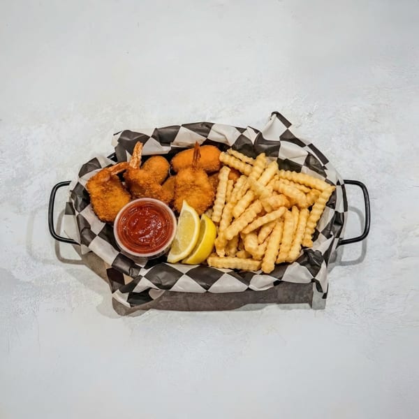 Fried shrimp, french fries, lemon wedges, and ketchup in a checkered paper-lined basket.