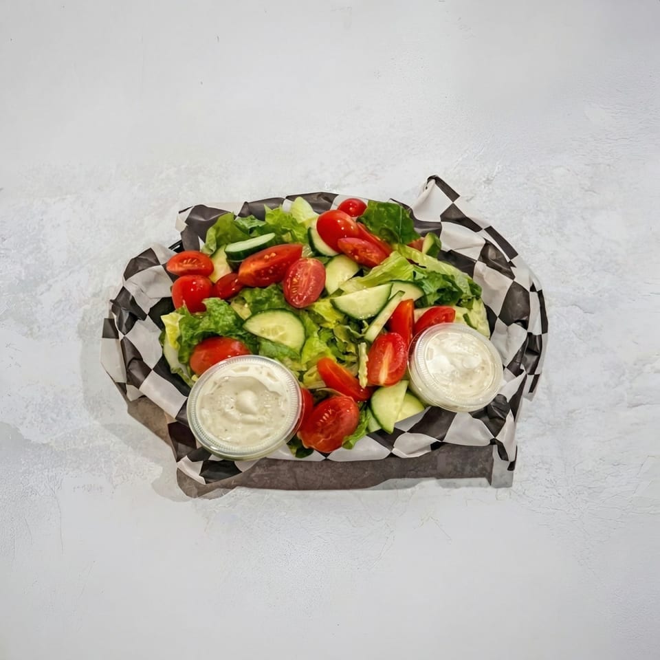 Fresh garden salad with lettuce, tomatoes, cucumbers, and two cups of dressing in a checkered paper-lined basket.