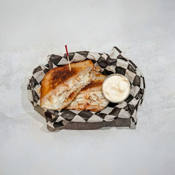 Grilled sandwich halves in a checkered paper-lined basket with a side of dipping sauce.