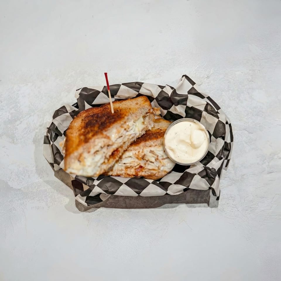 Grilled sandwich halves in a checkered paper-lined basket with a side of dipping sauce.