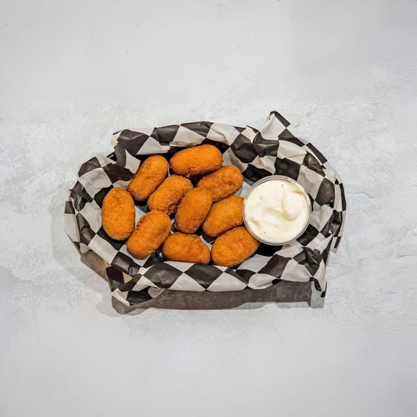 Golden-brown fried croquettes in a black and white checkered paper basket with a side of dipping sauce.
