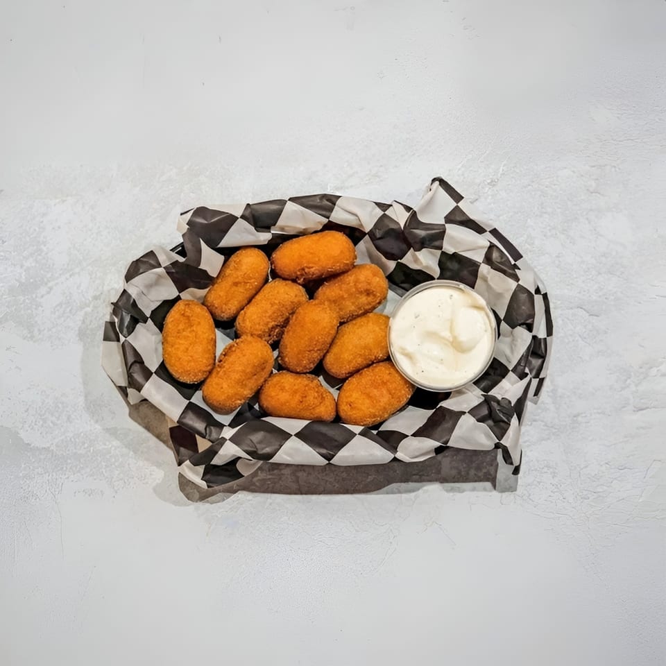 Golden-brown fried croquettes in a black and white checkered paper basket with a side of dipping sauce.