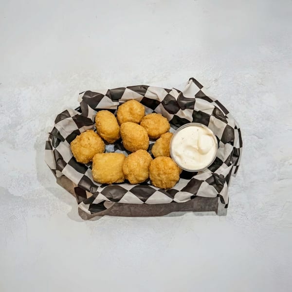 Golden-brown fried cheese curds in a black and white checkered paper-lined basket with a side of ranch.