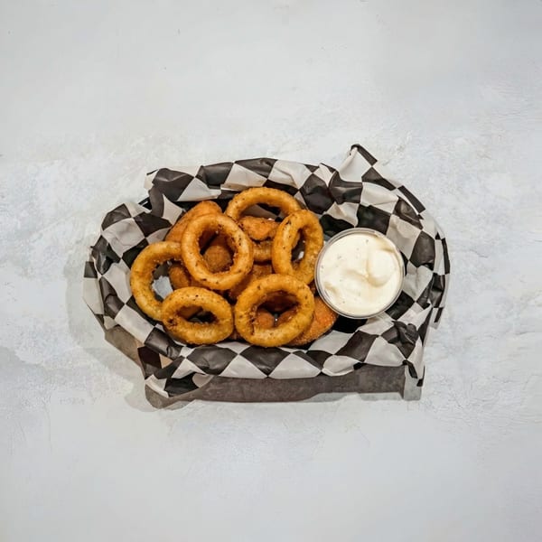 Golden-brown onion rings and a side of creamy dipping sauce in a checkered paper-lined basket.