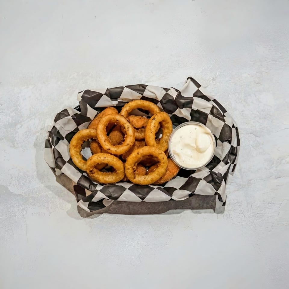 Golden-brown onion rings and a side of creamy dipping sauce in a checkered paper-lined basket.