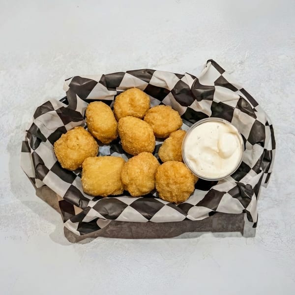 Golden-brown fried cheese curds in a black and white checkered paper-lined basket with a side of dipping sauce.