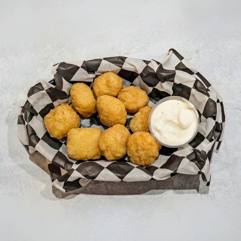 Golden-brown fried cheese curds in a black and white checkered paper-lined basket with a side of dipping sauce.