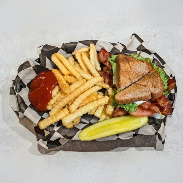 A club sandwich with fries, ketchup, and a pickle spear in a checkered paper-lined basket.